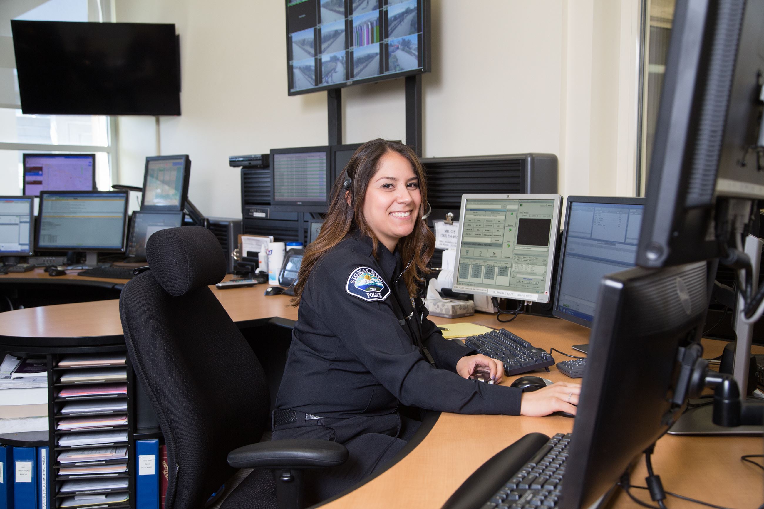 Smiling police dispatcher at a desk with a headset on