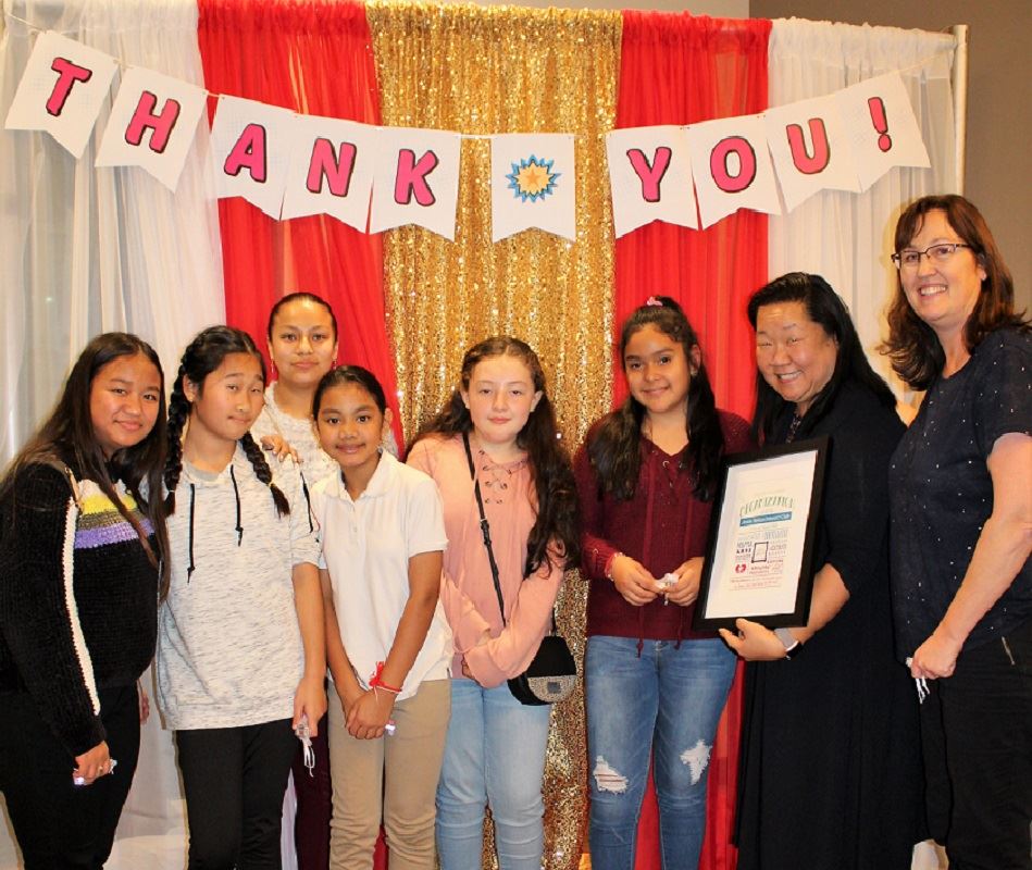 Six young students and two adult teachers standing in front of a Thank You sign and holding an award